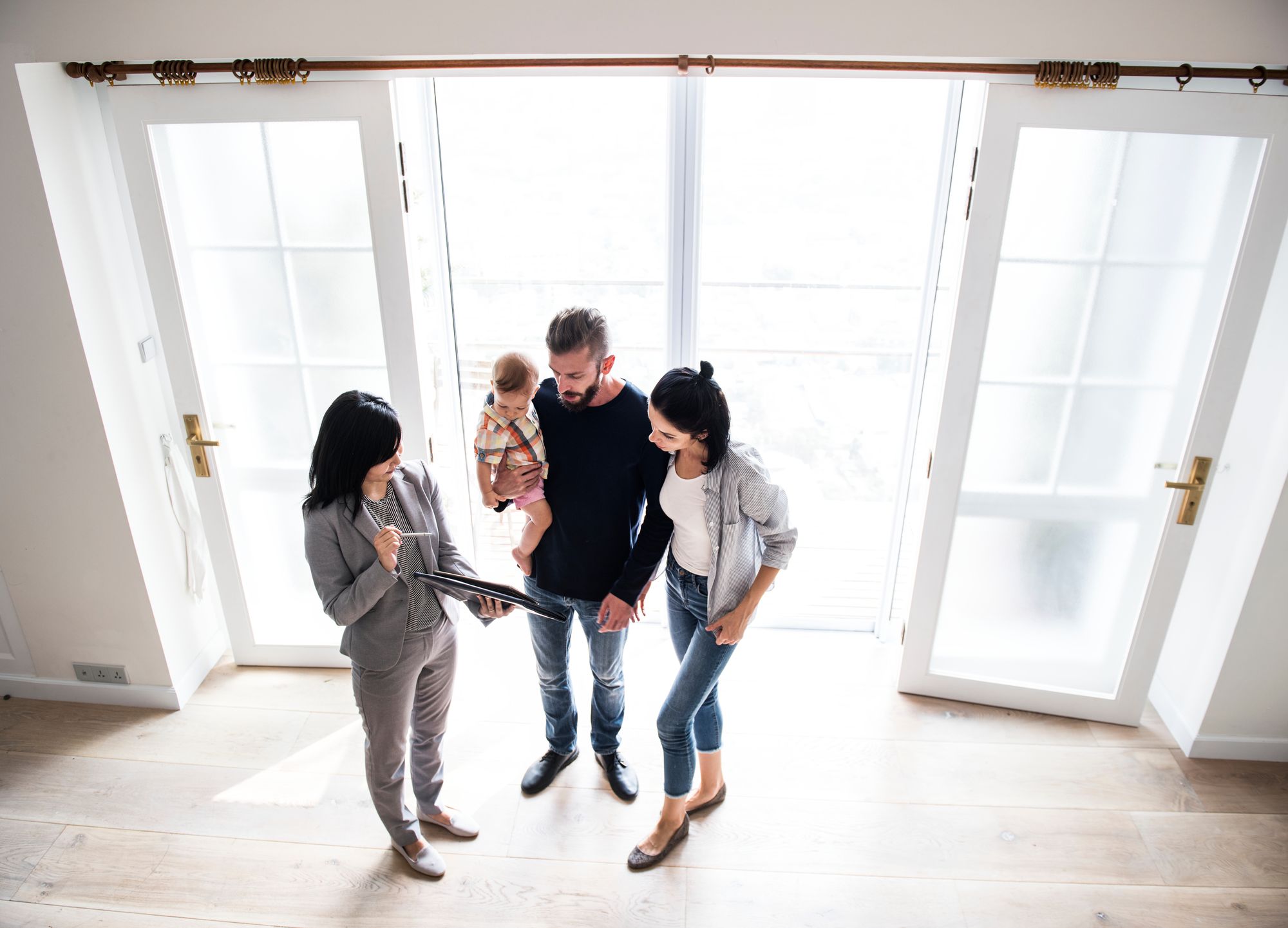 A REALTOR shows a home to a young family while gesturing to a document within a portfolio.